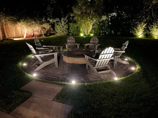 15-foot gravel fire pit patio area with poly-resin Adirondack chairs and string lights at dusk