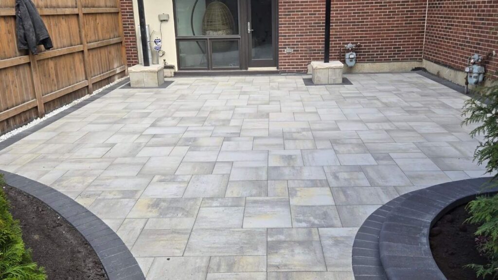 A newly paved patio with curved garden beds and a brick building.