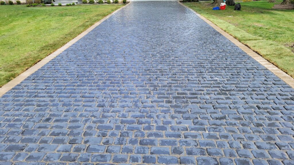 A newly paved driveway with dark gray cobblestones and a tan border.