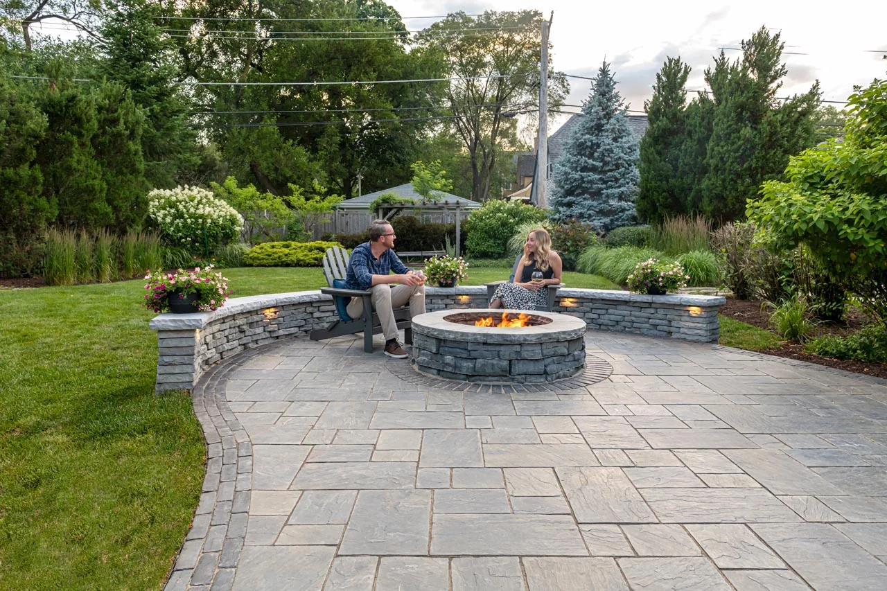 Premium Unilock stone seating wall with integrated LED under-cap lighting around a custom stone fire pit Premium Unilock stone seating wall with integrated LED under-cap lighting around a custom stone fire pit