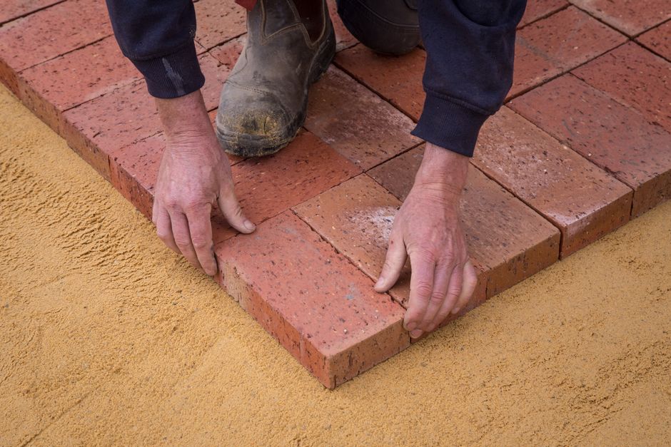 A professional contractor screeding sand for a concrete paver walkway