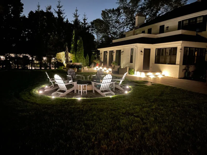 A custom-designed brick fire pit patio featuring built-in seating walls and landscape lighting