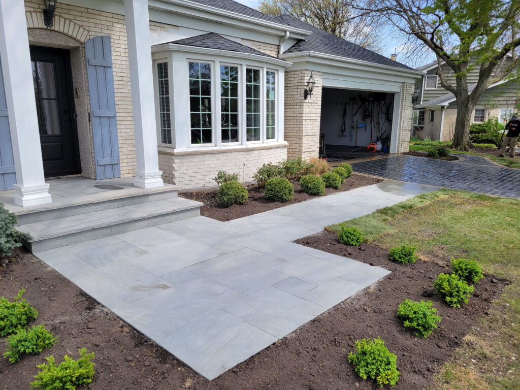 Newly paved brick walkway and landscaped front entry beside a brick house