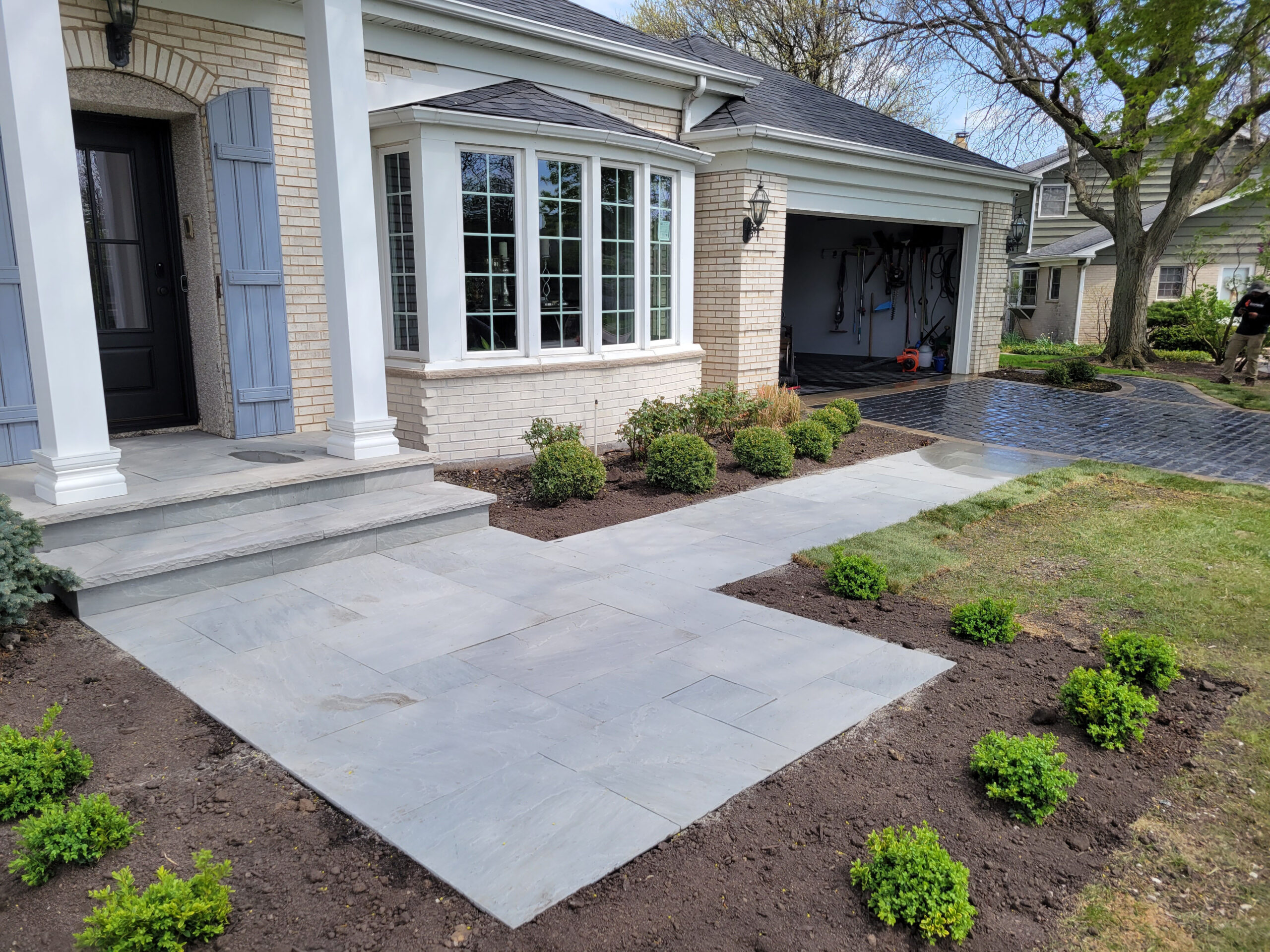 Newly paved brick walkway and landscaped front entry beside a brick house